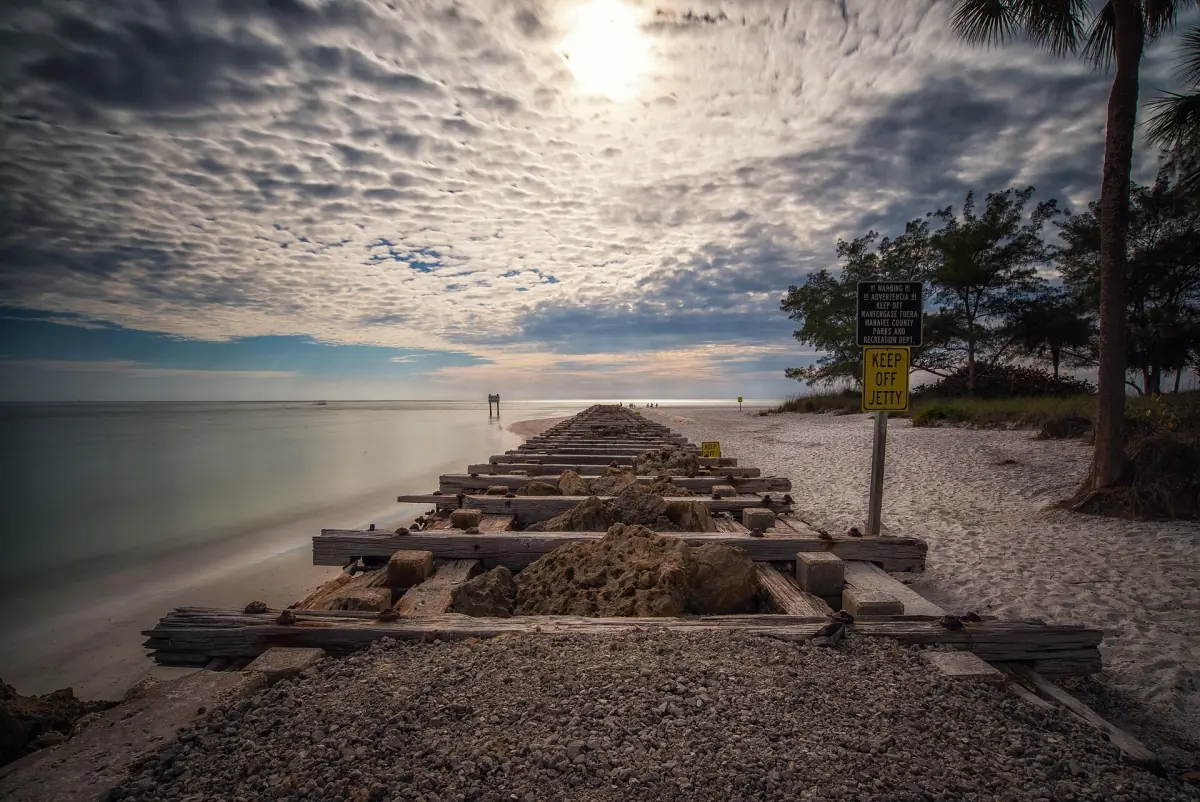 Old wooden jetty pilings leading into calm Gulf water under cloudy sky