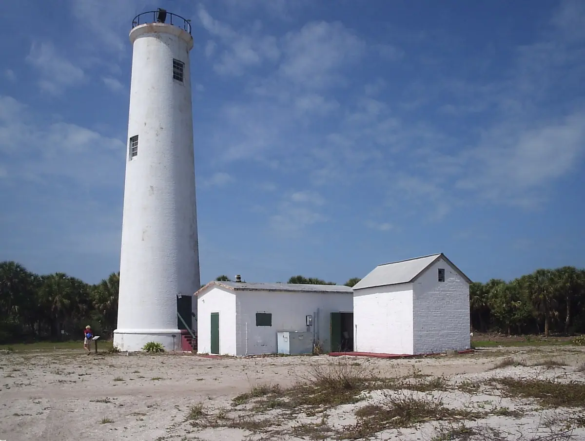 White lighthouse tower with a small outbuilding on sandy ground
