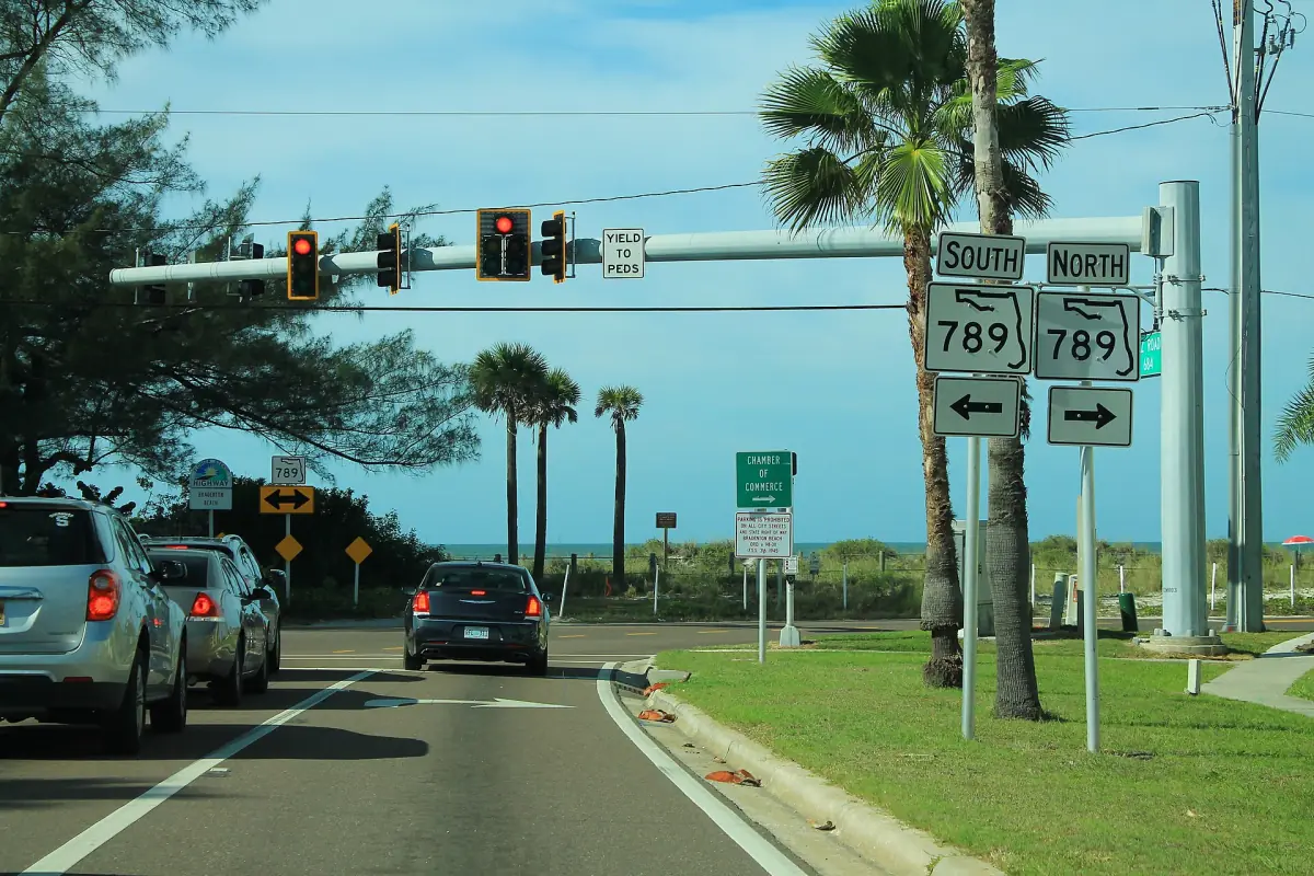 Road junction with state route signs and palm trees leading toward the beach