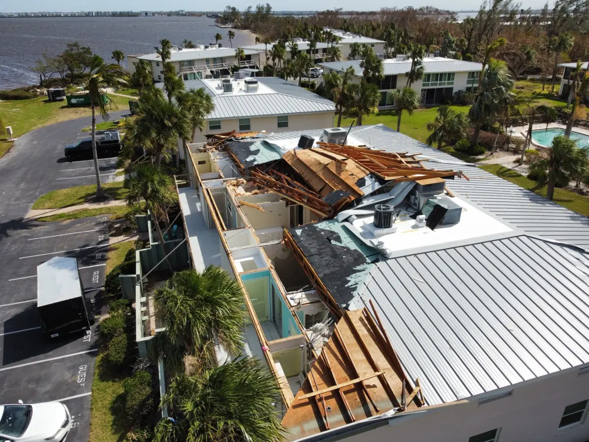 Aerial view of a damaged apartment roof beside palm trees
