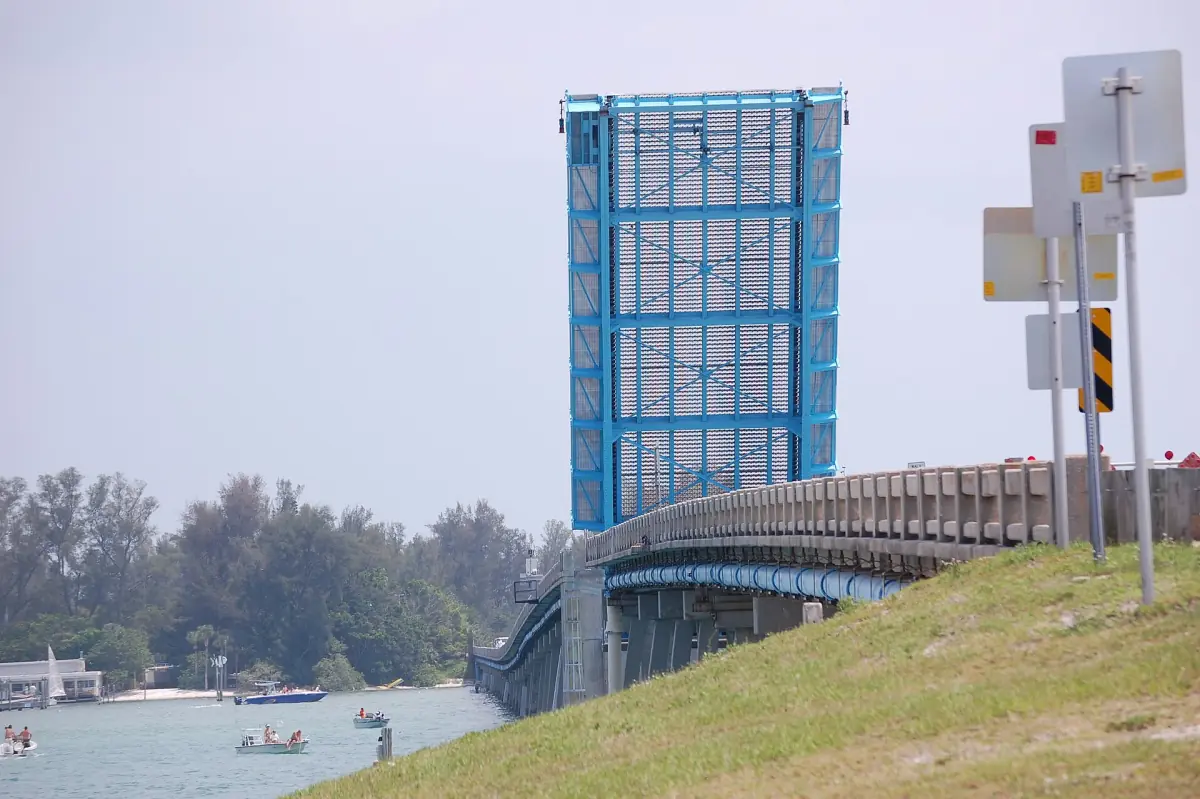 Drawbridge span raised above a pass with boats and a blue sky